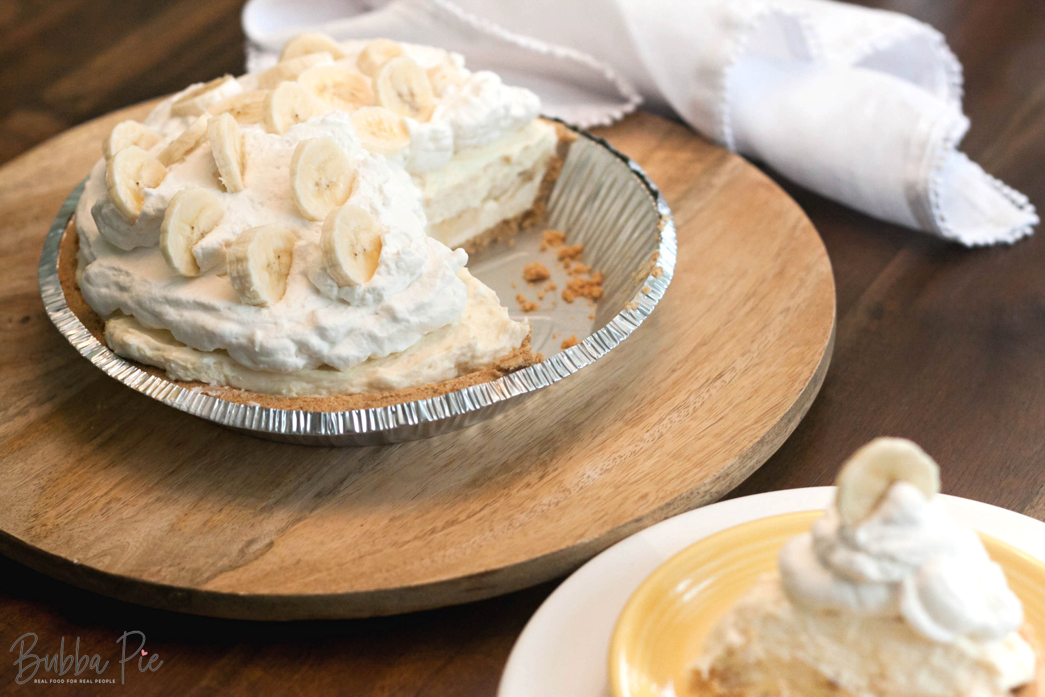 Easy No Bake Banana Cream Pie slice sitting on a plate with fresh bananas and whipped cream on top.