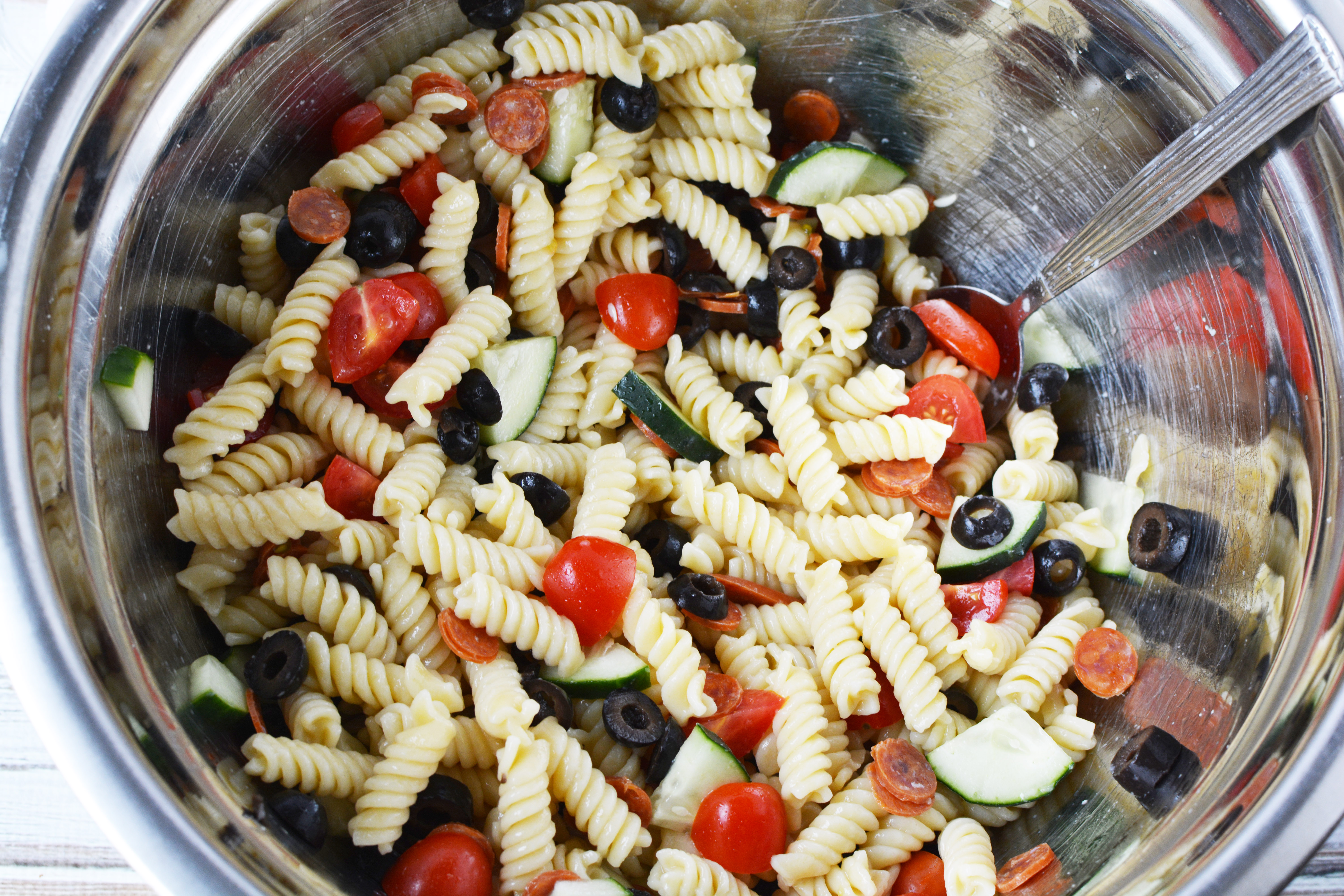 rotini salad being mixed with Italian salad dressing in a bowl.