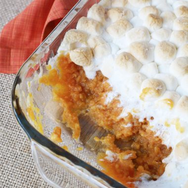 a dish of Sweet Potato casserole with marshmallows on top sitting on a counter with an orange napkin