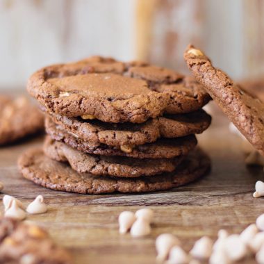 Salted Caramel Chocolate Cookies sitting on a table with chocolate and caramel chips