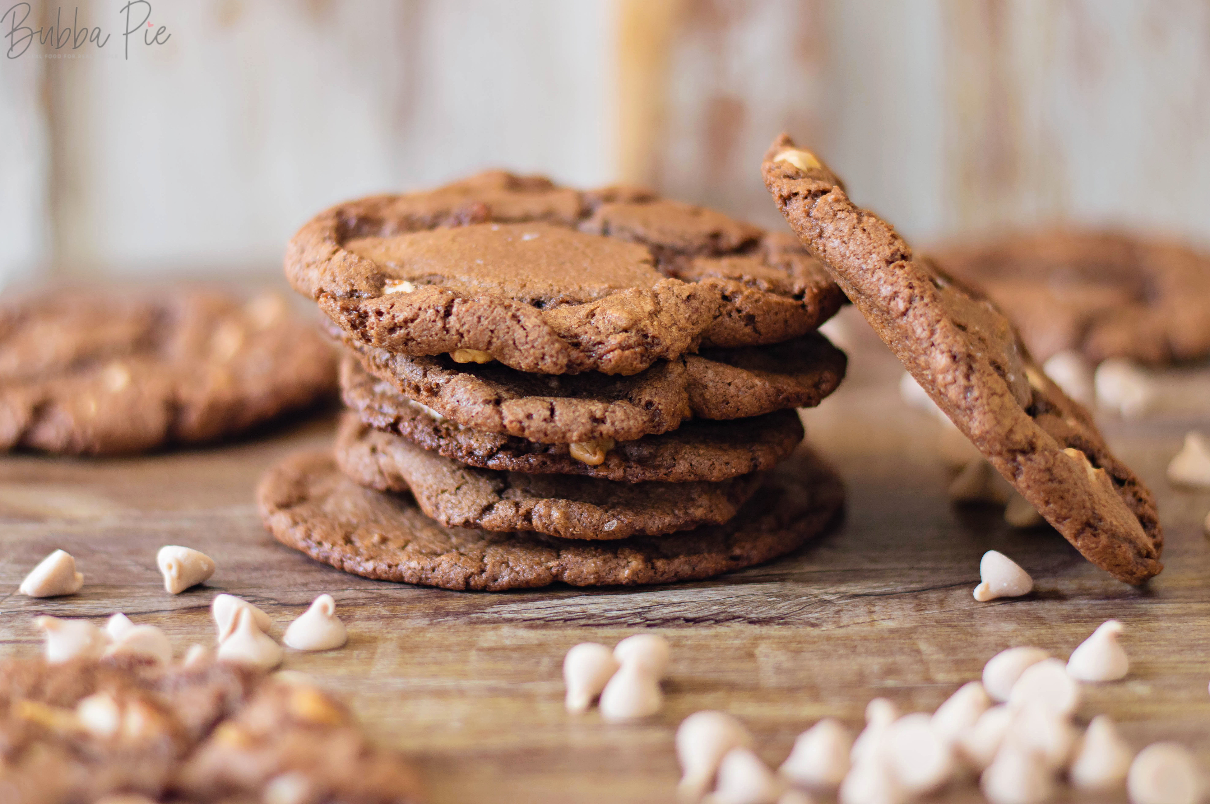 Salted Caramel Chocolate Cookies sitting on a table with chocolate and caramel chips