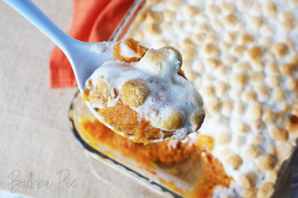a spoon full of Sweet Potato casserole with marshmallows hovering over the casserole dish