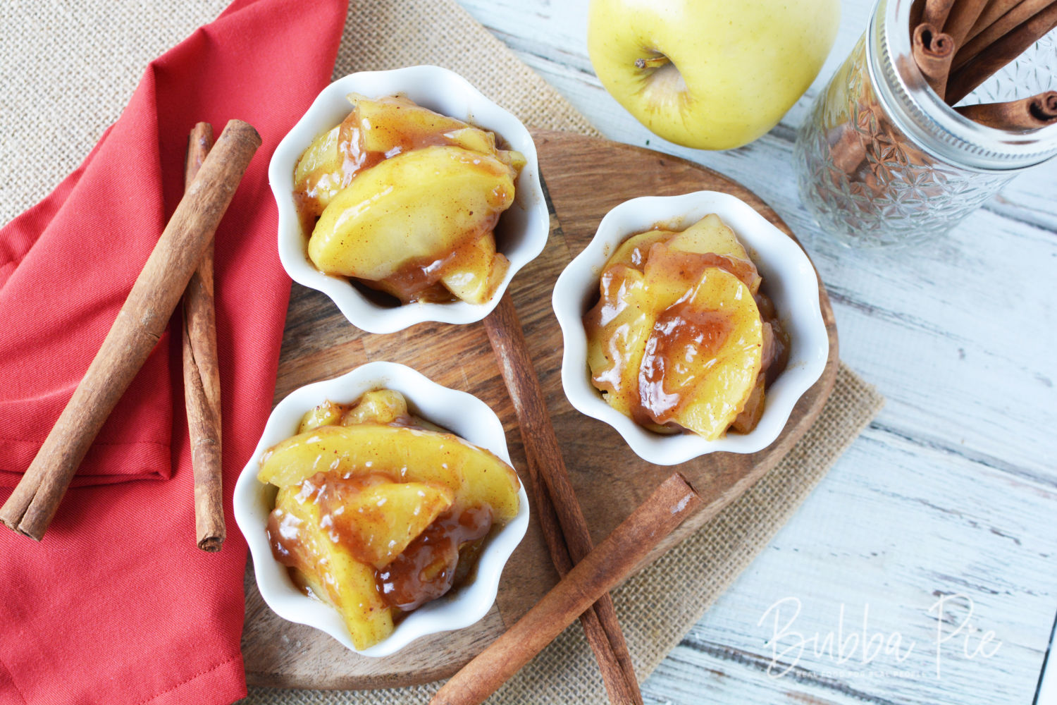 small white bowls of fried apples on a cutting board with a red napkin and cinamon sticks