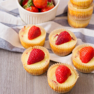 Mini Strawberry Cheesecake Bites sitting on a table with fresh strawberries.
