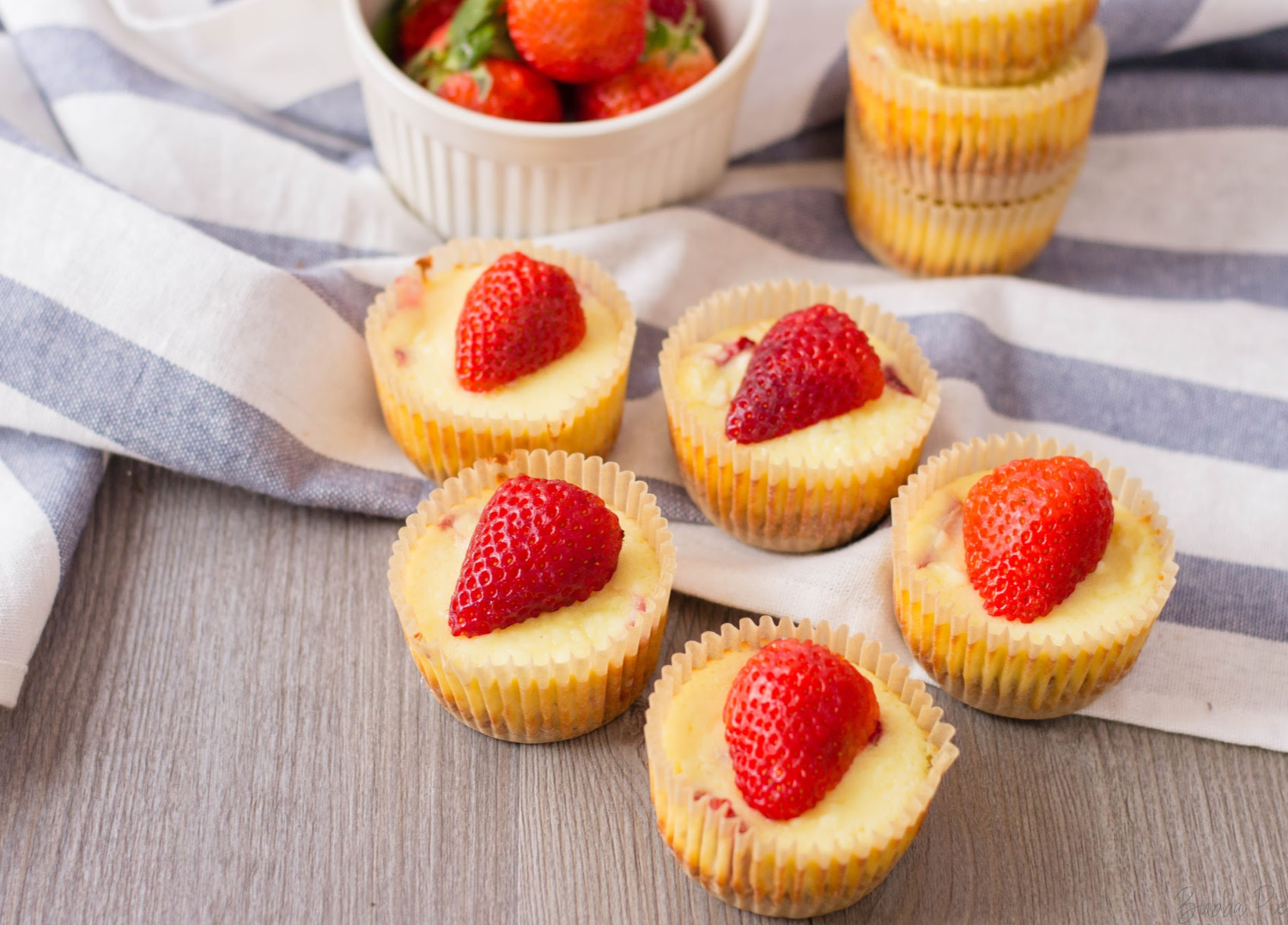 Mini Strawberry Cheesecake Bites sitting on a table with fresh strawberries. 