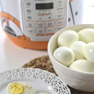A hard boiled egg sitting on a plate in front of a bowl of hard boiled eggs and a Star Wars themed Instant Pot
