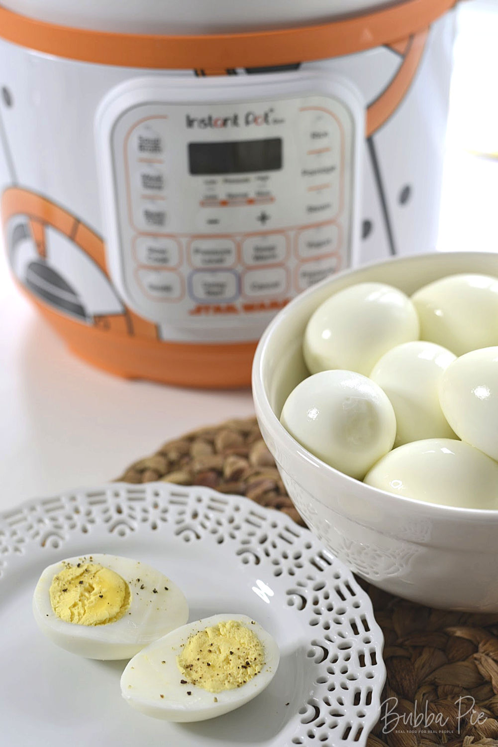 A hard boiled egg sitting on a plate in front of a bowl of hard boiled eggs and a Star Wars themed Instant Pot