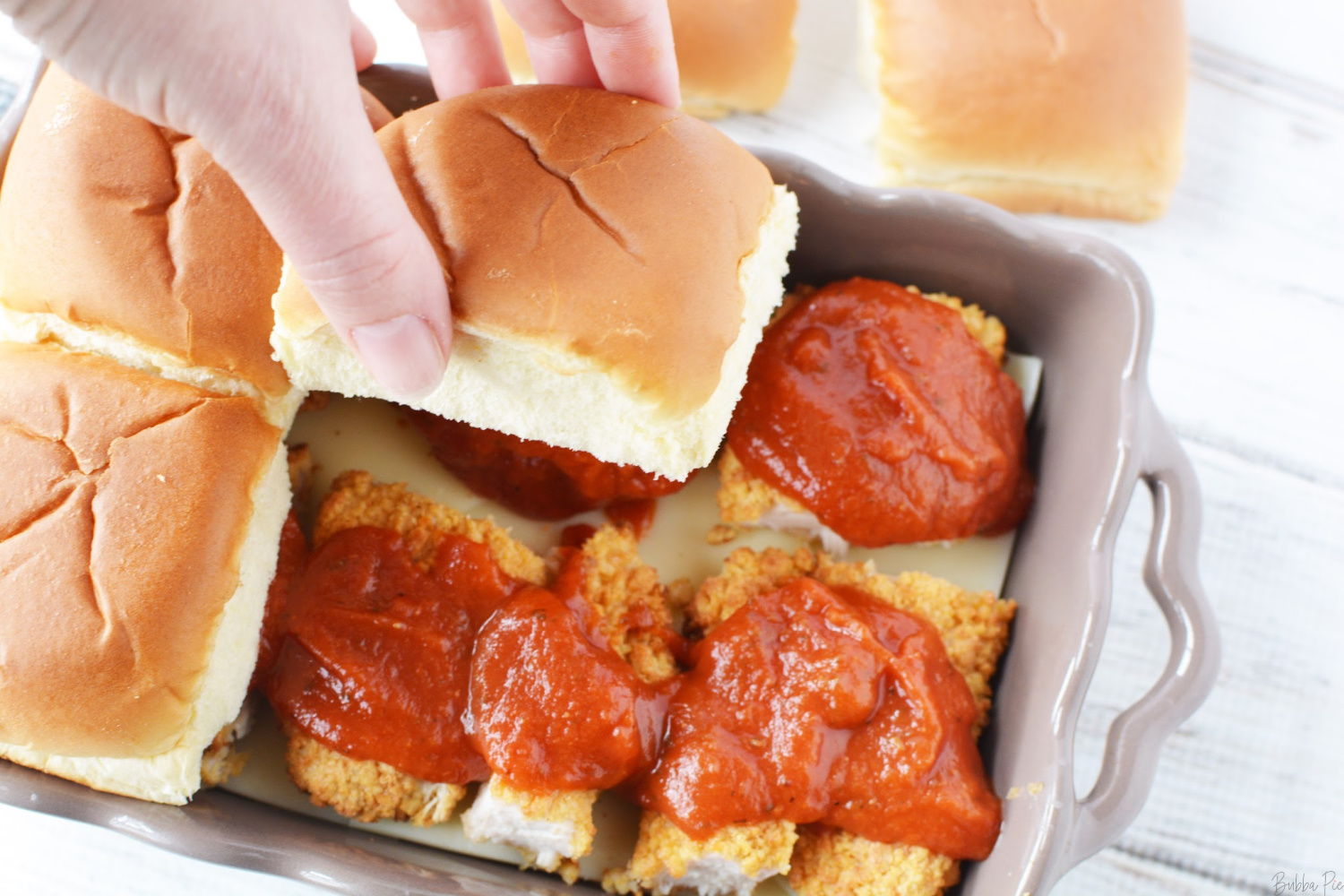 Easy Chicken Parmesan Sliders are covered with provolone cheese and marinara sauce before going on the oven.