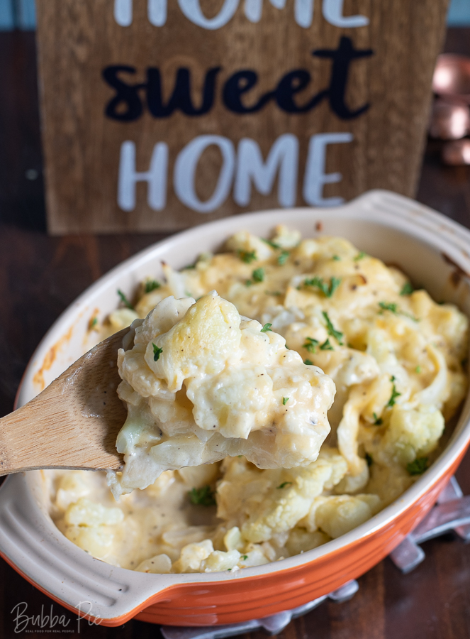 Baked Cheesy Cauliflower being put on a dinner plate with a wooden spoon