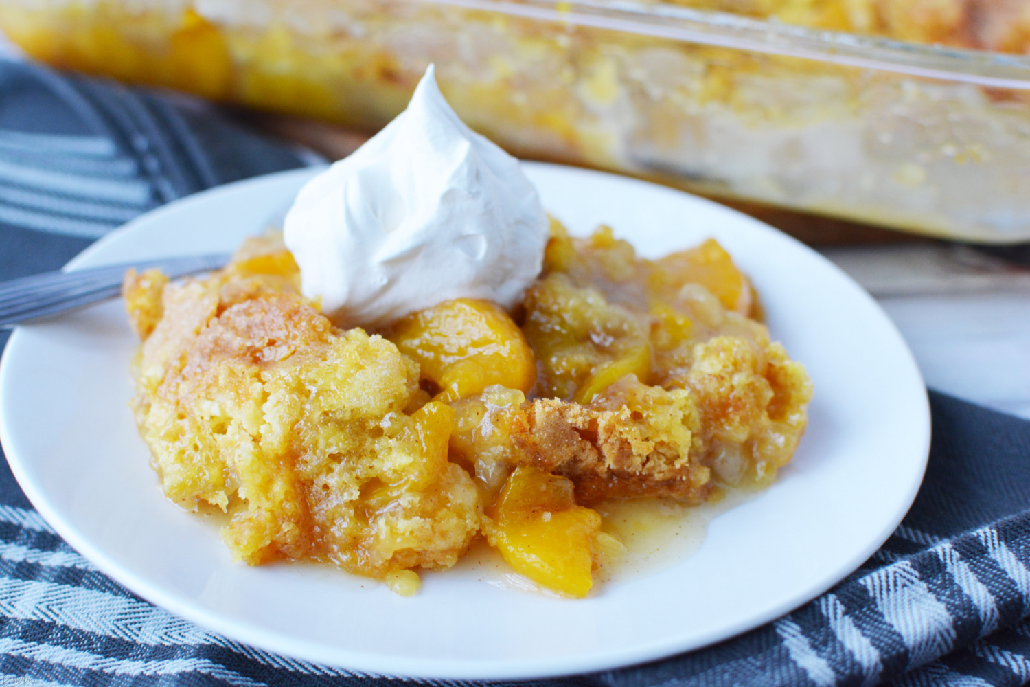 Easy Peach Cobbler with Cake Mix on a white plate with whipped cream on top