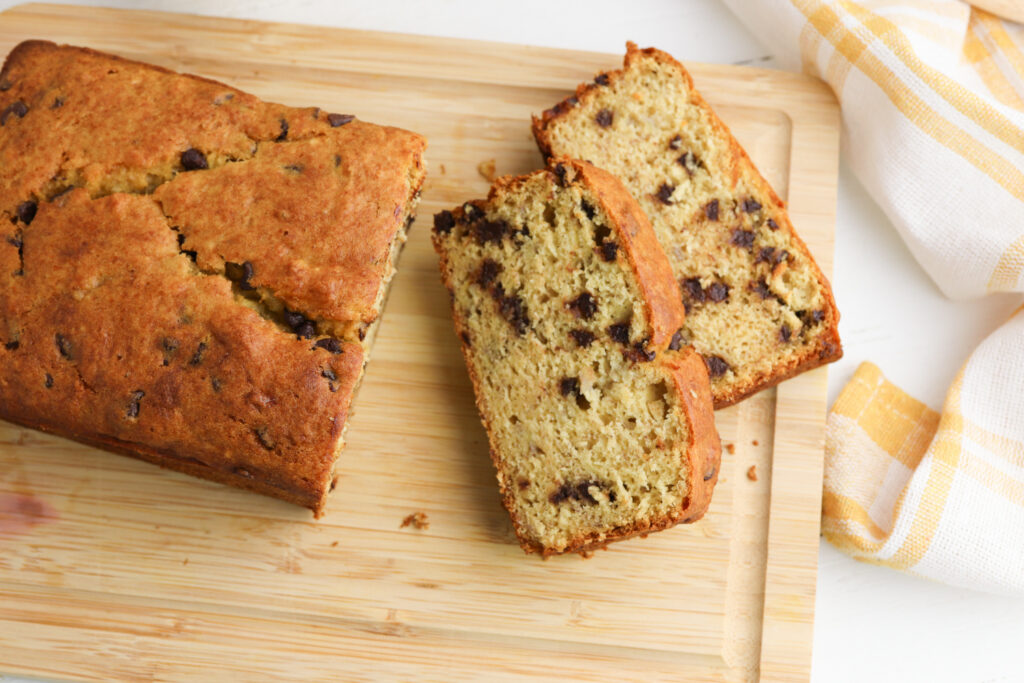 banana bread being sliced on a cutting board.