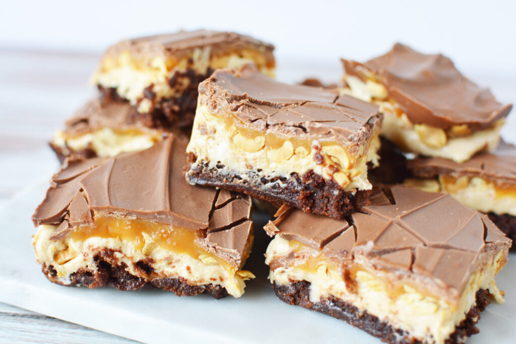 Snickers Brownies stacked on a plate.