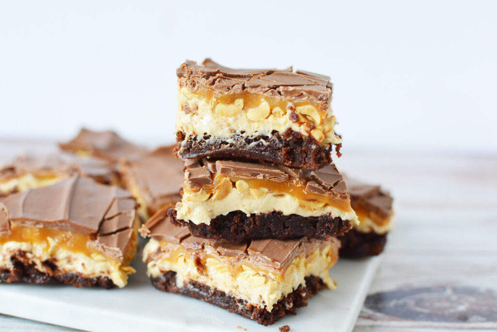 Snickers Brownies stacked together on a plate.