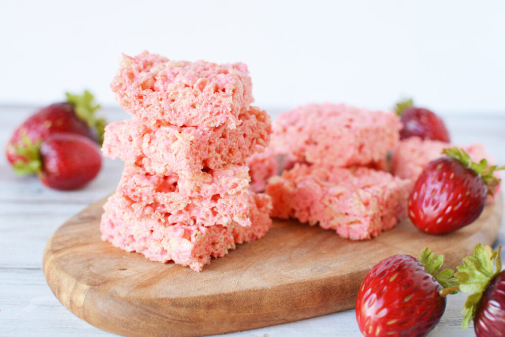 Strawberry Rice Krispies Treats laying on a platter with strawberries.