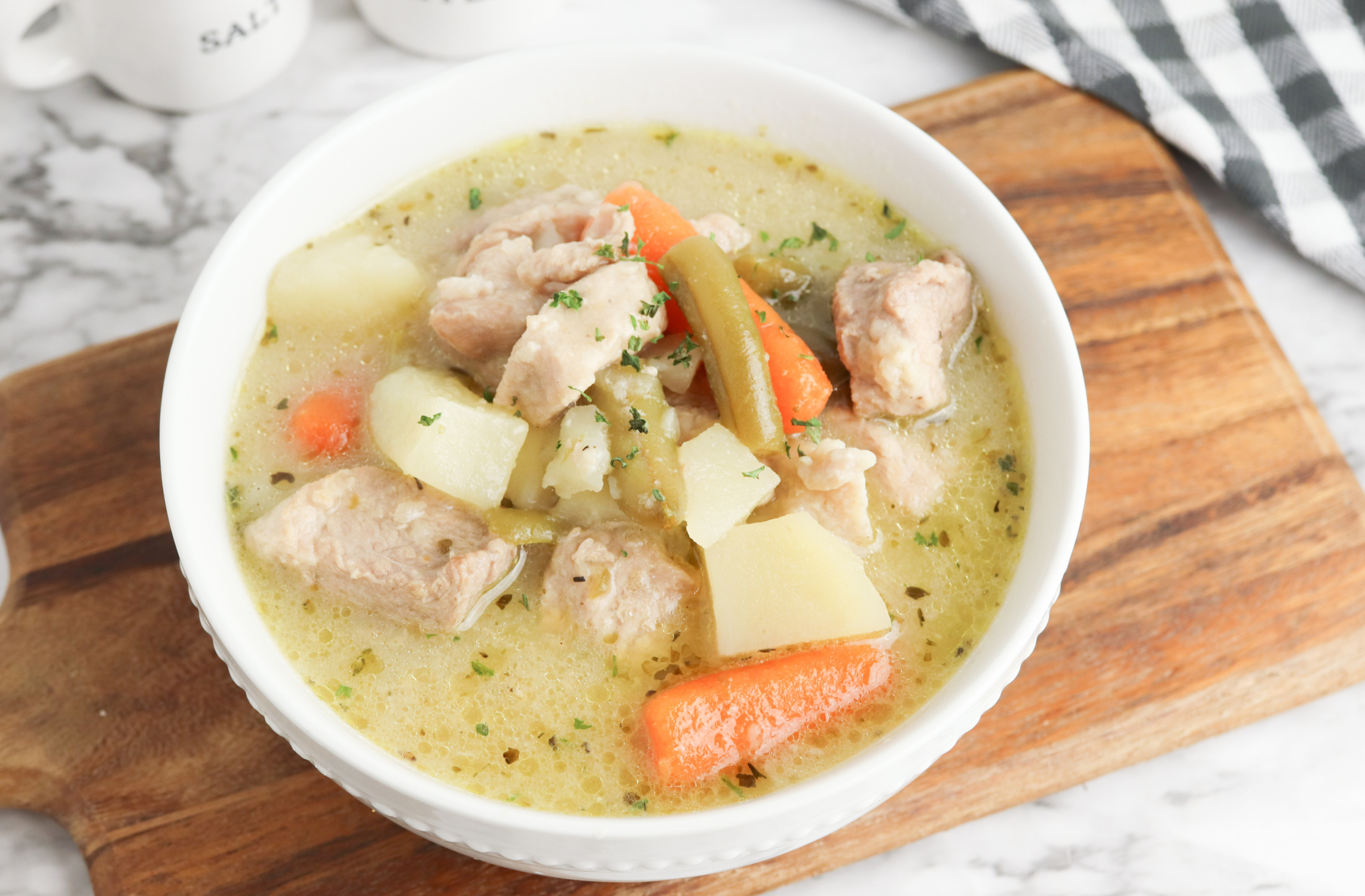 pork stew served in a white bowl on a wooden board