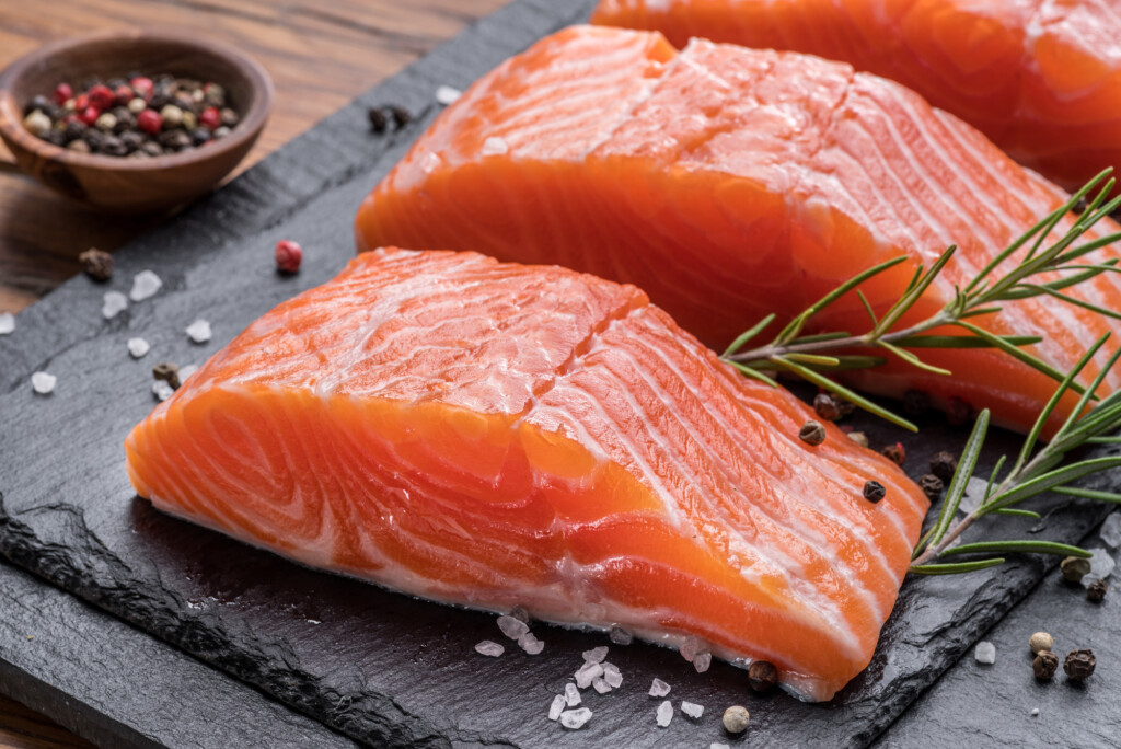 Fresh salmon fillets on black cutting board.